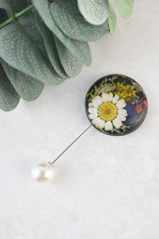 Melna apaļa piespraude ar ziediem